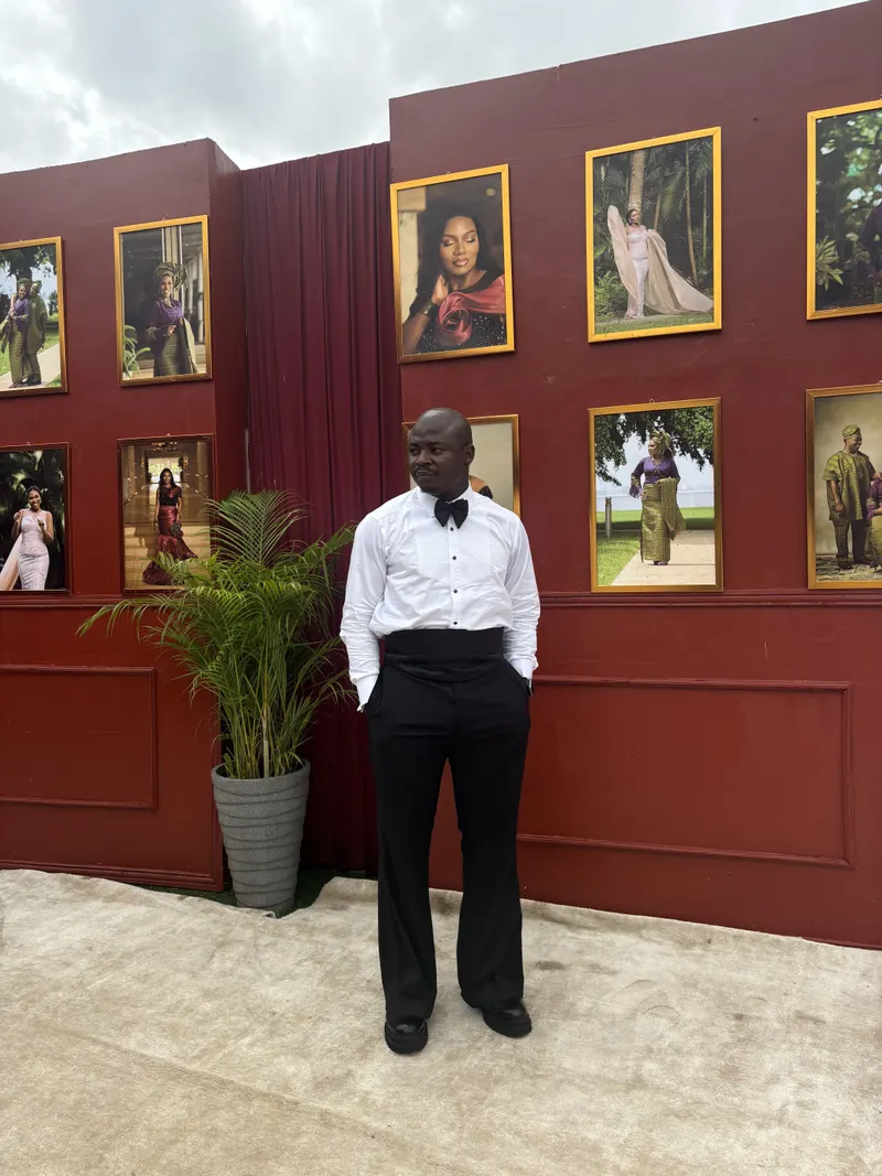 The Corporate Emcee in a white shirt and bow tie beside a wall of framed portraits at a celebration