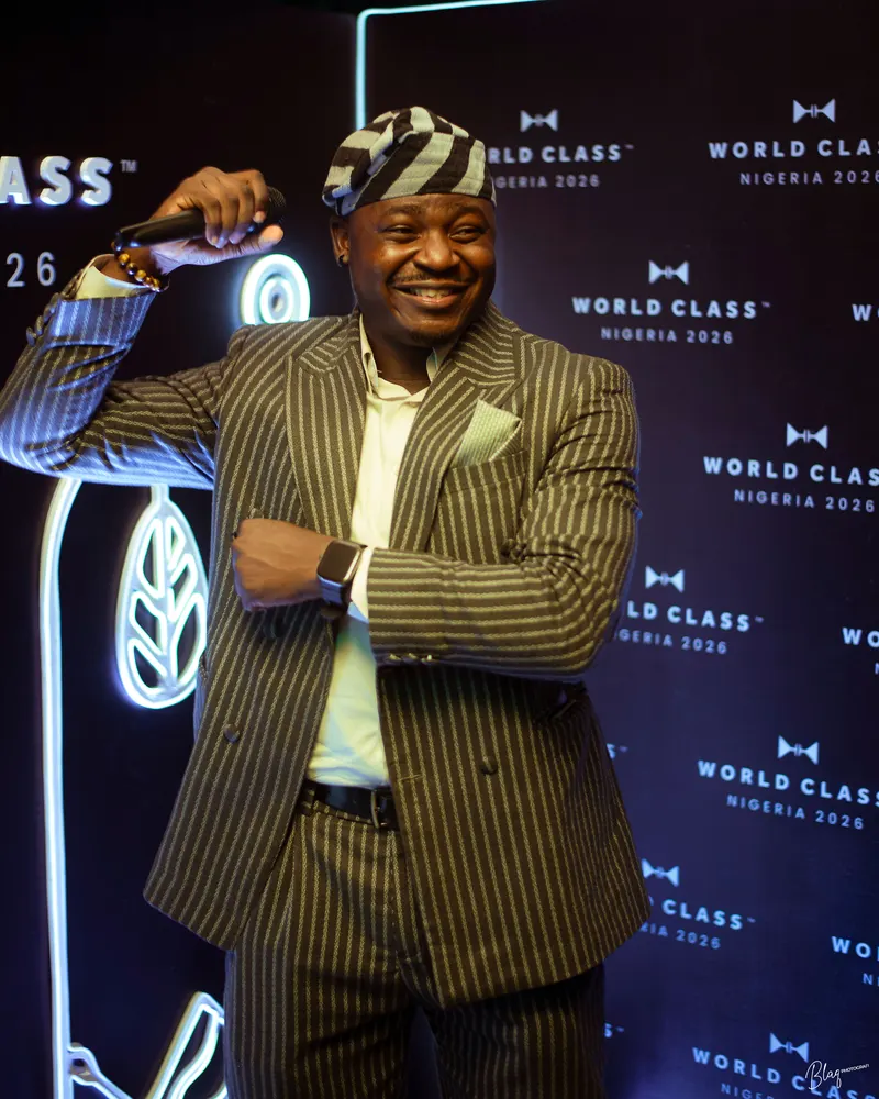 The Corporate Emcee raising his microphone in front of the World Class Nigeria 2026 backdrop