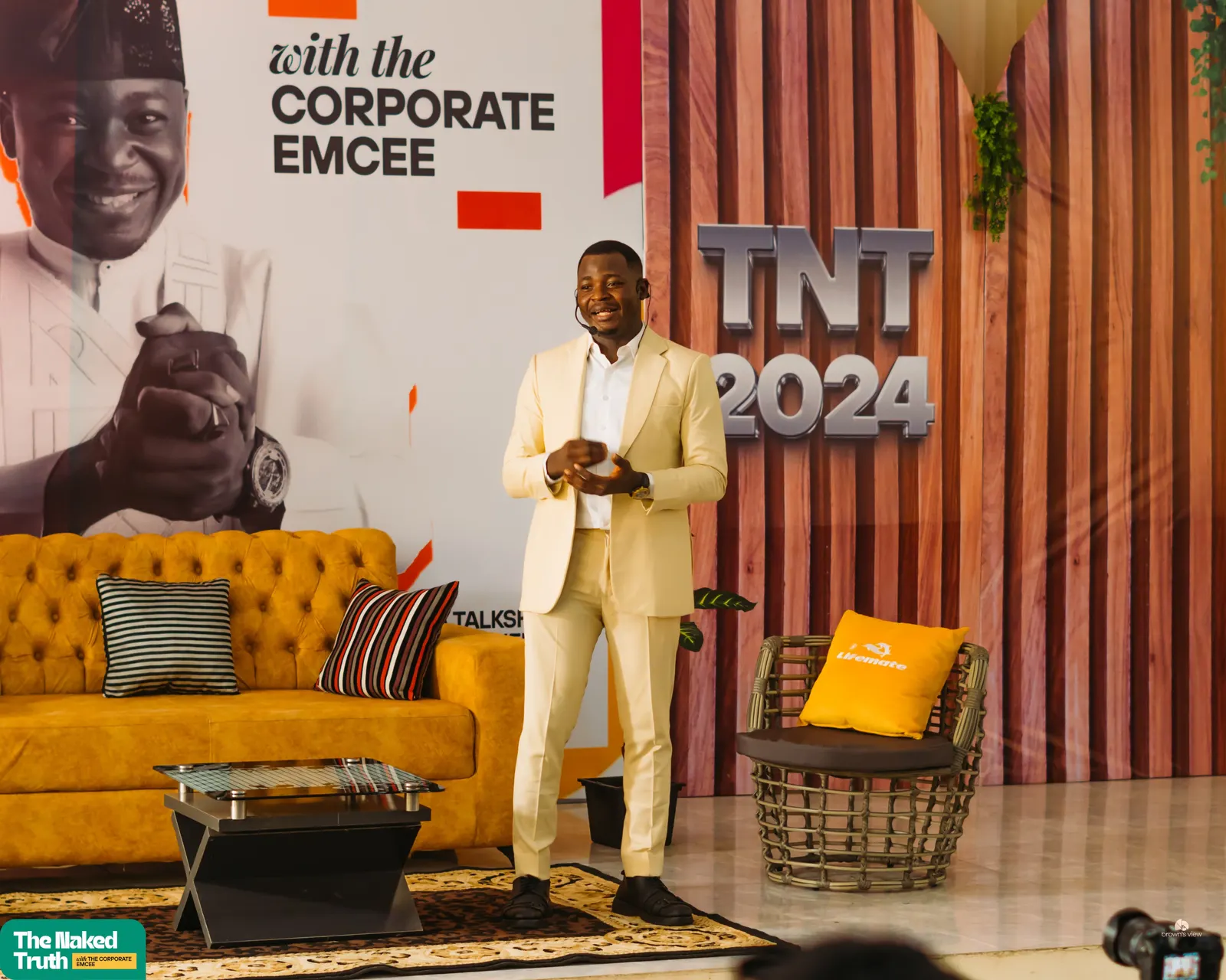 The Corporate Emcee in a cream suit hosting The Naked Truth talk show, TNT 2024
